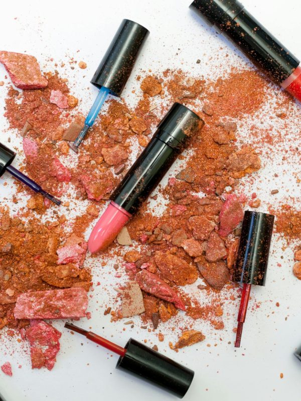 Colorful scattered makeup products including lipsticks and crushed powders on a white background.